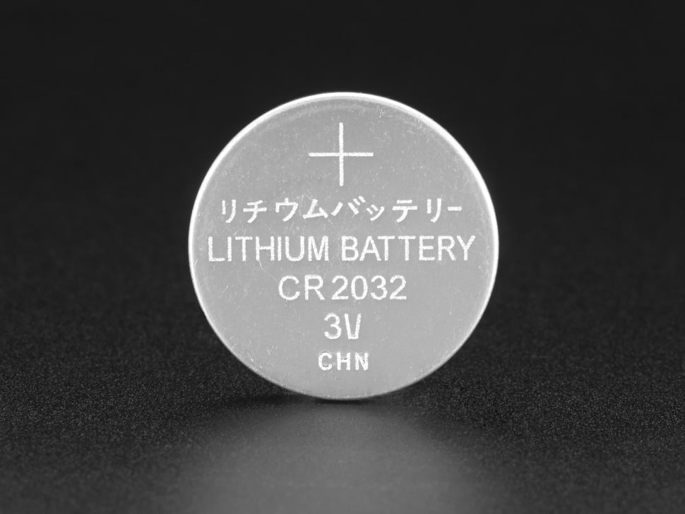 A CR2032 coin-cell battery sitting next to a small screwdriver on a garage workbench