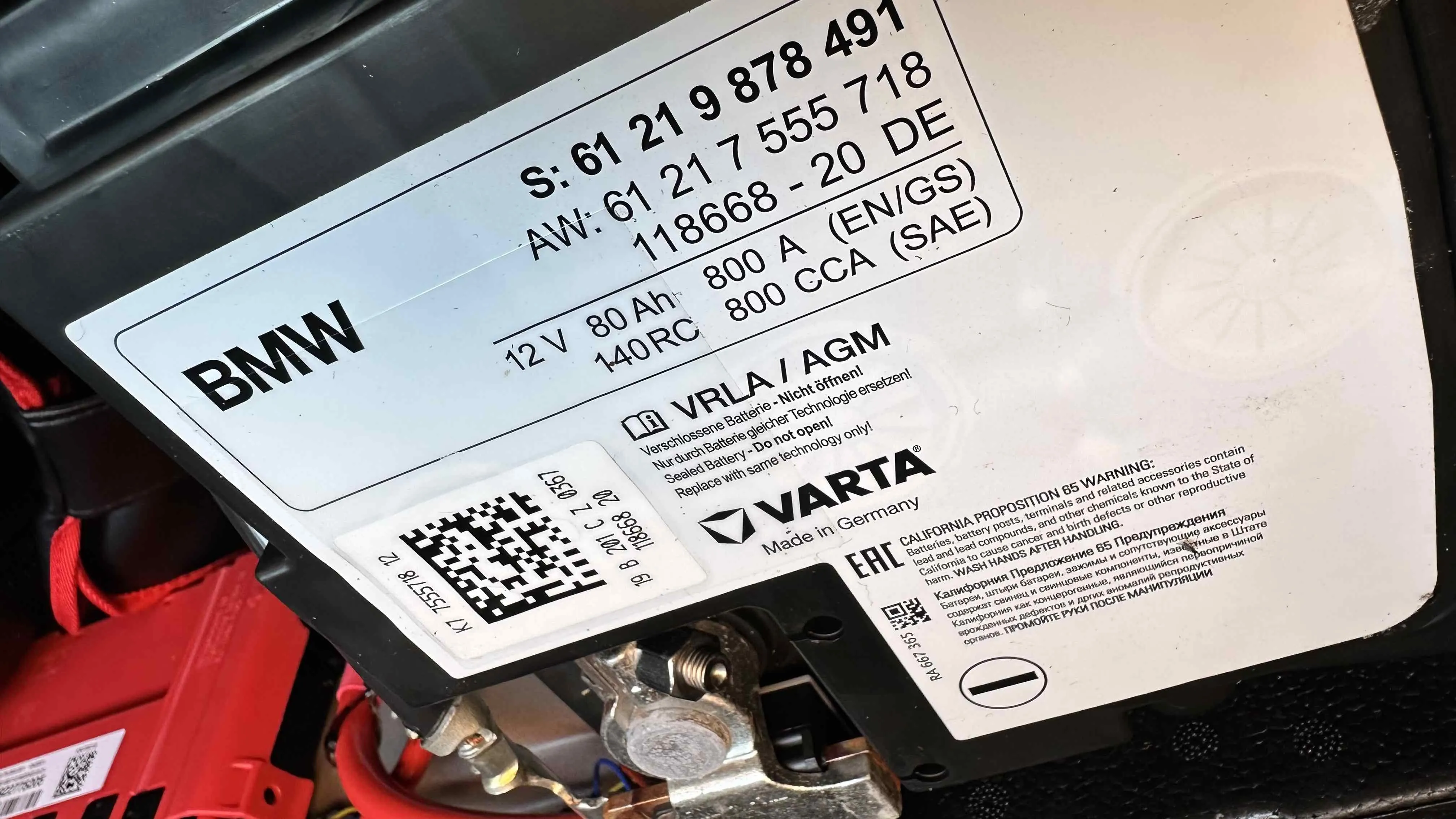 A close-up photo of an AGM car battery label showing the battery type and amp-hour rating printed on the top case