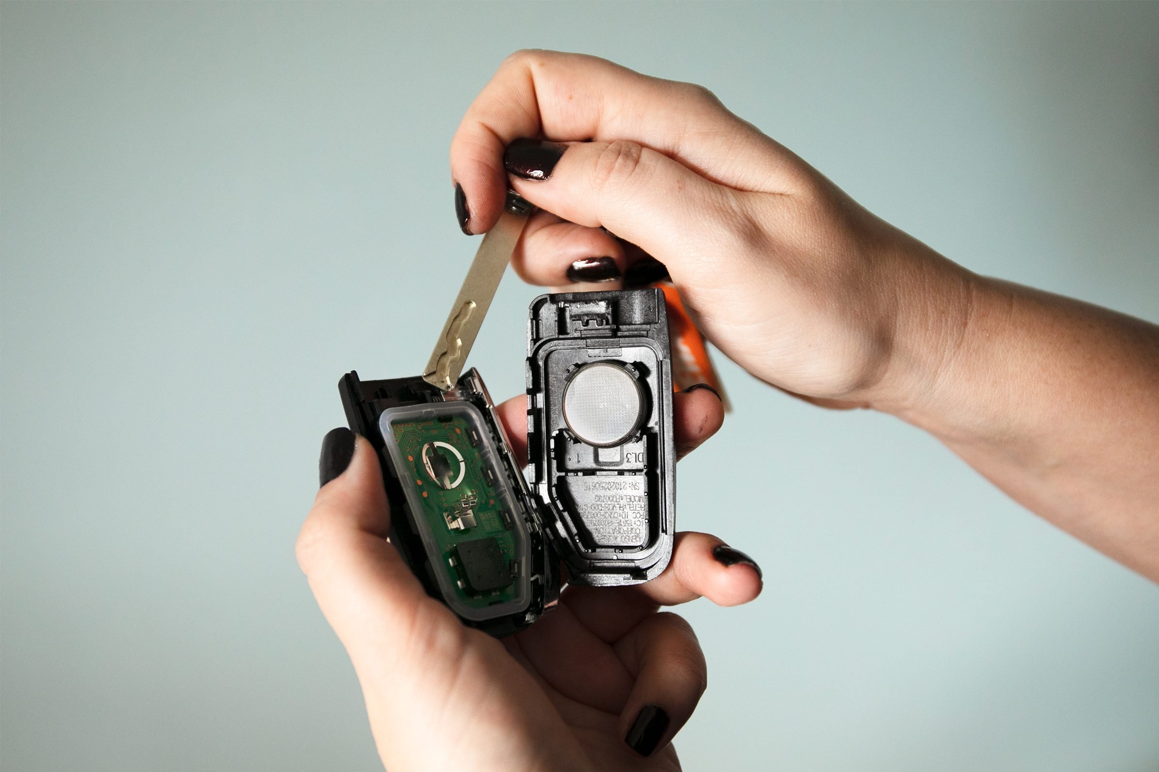 A modern car key fob opened on a workbench with a coin-cell battery visible inside