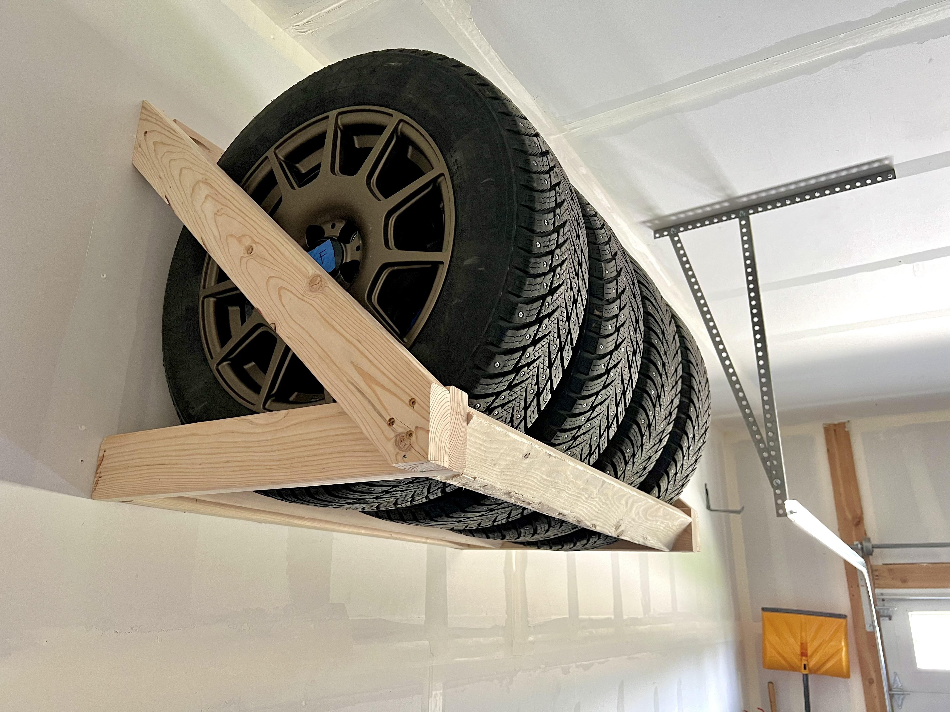 A set of four clean mounted wheels in protective tire bags stacked neatly in a cool, shaded corner of a residential garage, with no sunlight hitting the tires
